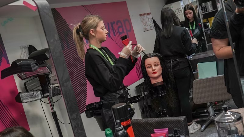 A student practising styling hair on a professional styling head at the Wheeler Gate salon.