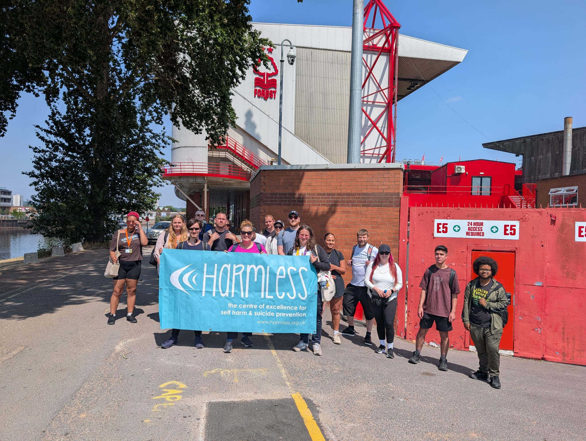 Staff and students outside City Ground holding a banner that has the charity Harmless text written on it