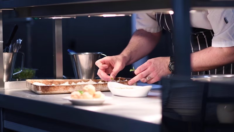 A student garnishing a dish on the pass at the training kitchen at the City Hub.