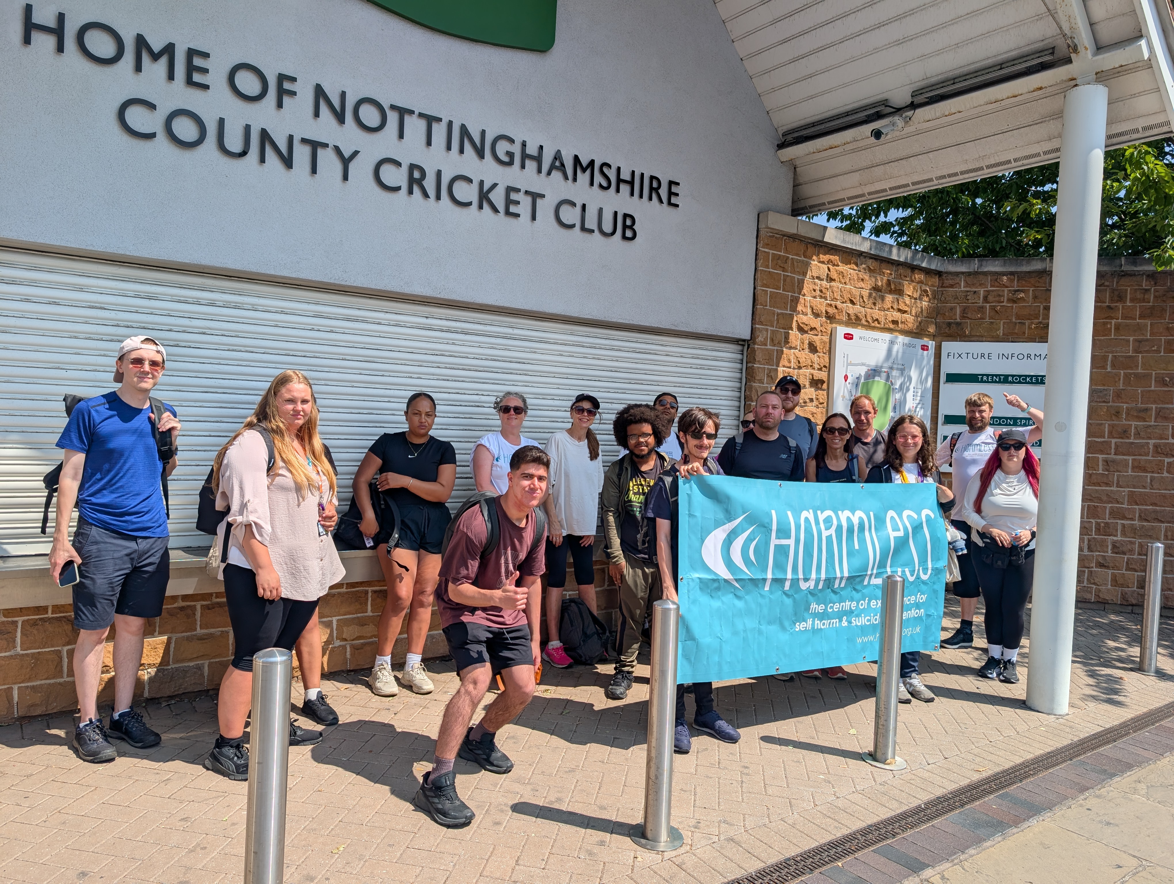 Staff and students outside Cricket Club holding a banner that has the charity Harmless text written on it