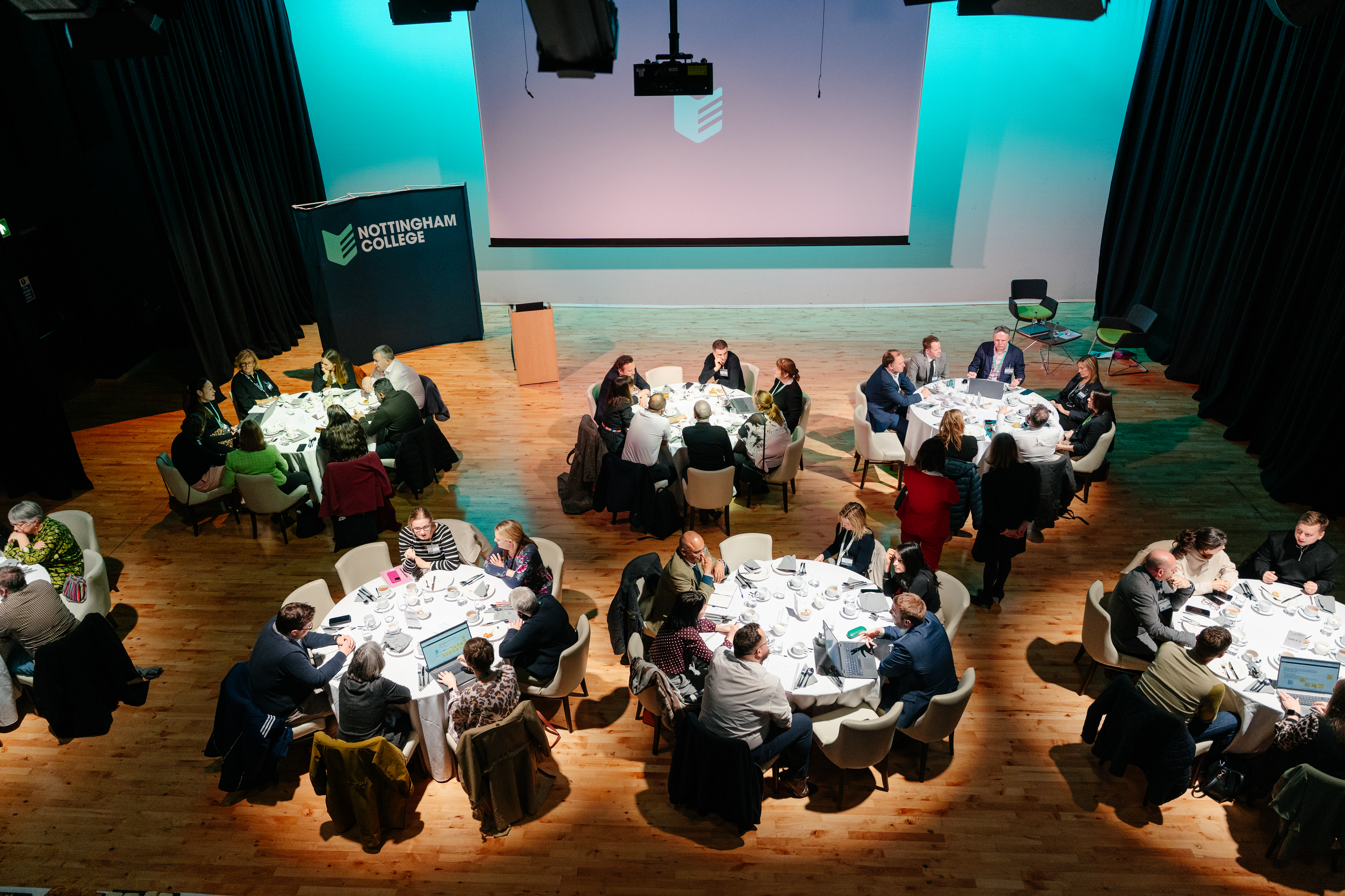 Delegates and stakeholders sitting at tables inside the Fletchers Theatre.