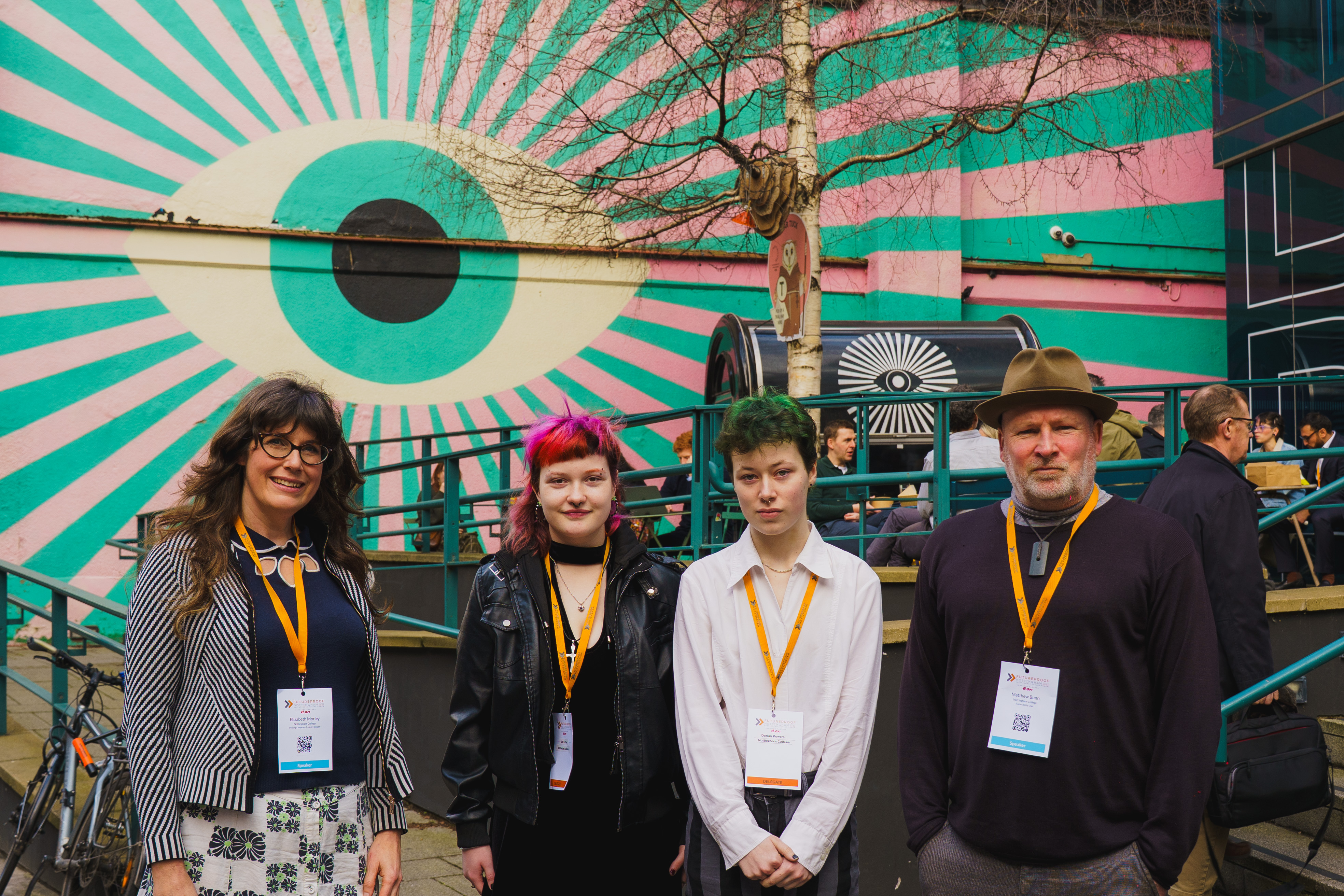 Liz and Matt stand in a line with two students in the centre, they are pictured outside Broadway Cinema with a mural of a pink and green eye behind them.