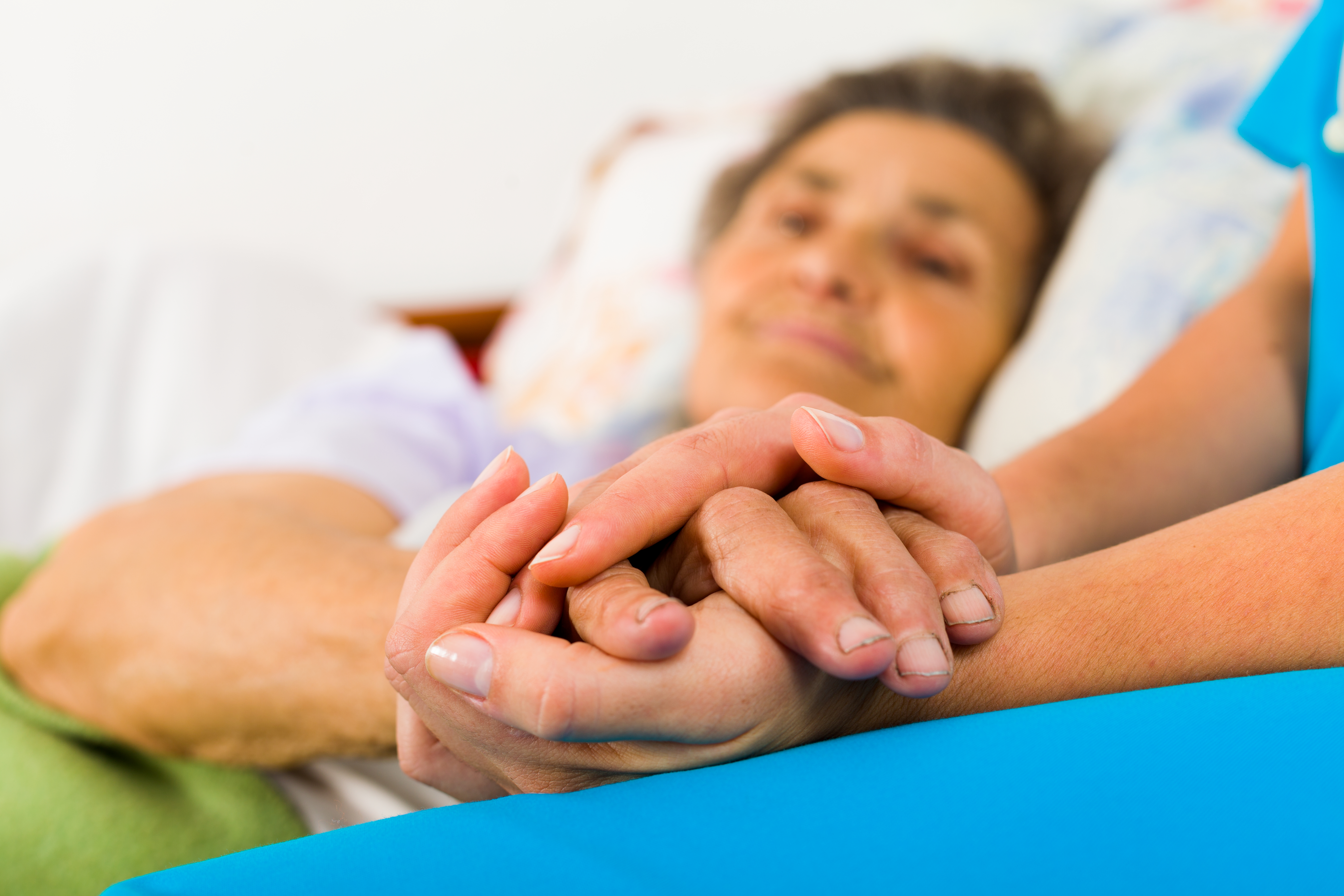 Patient in a bed holding hands with a nurse
