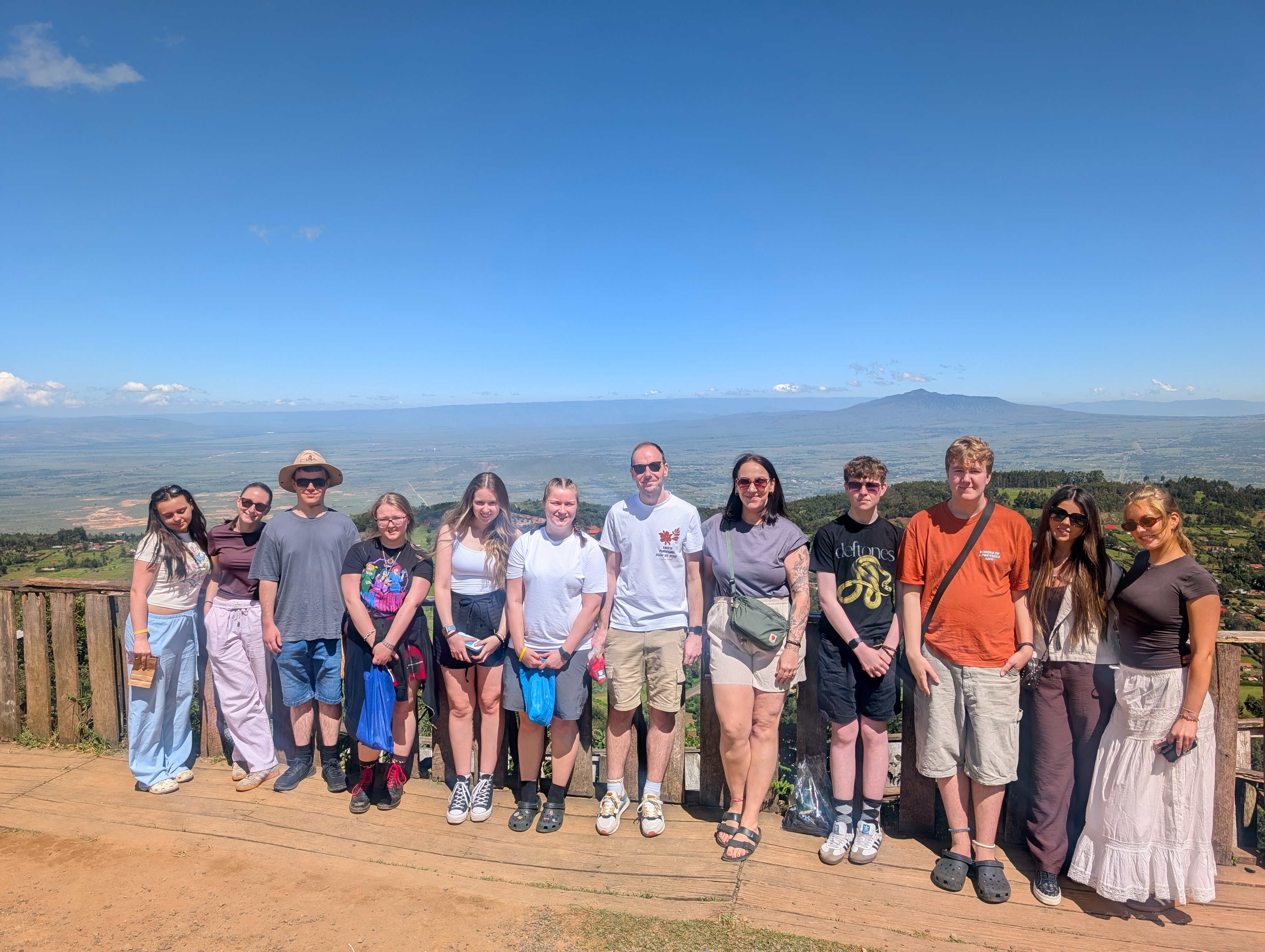 Photograph of 12 students standing in front of a fence with a vast landscape in the background.