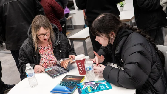 Two people at Open Evening sitting in the canteen with items on the table