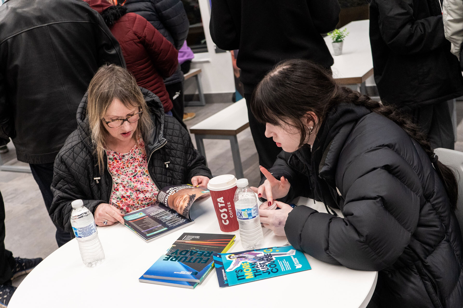 Two students sitting at a table with a coffee at an open evening.