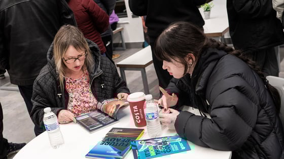 Two students sitting around a table with a coffee looking at brochures at an open evening.