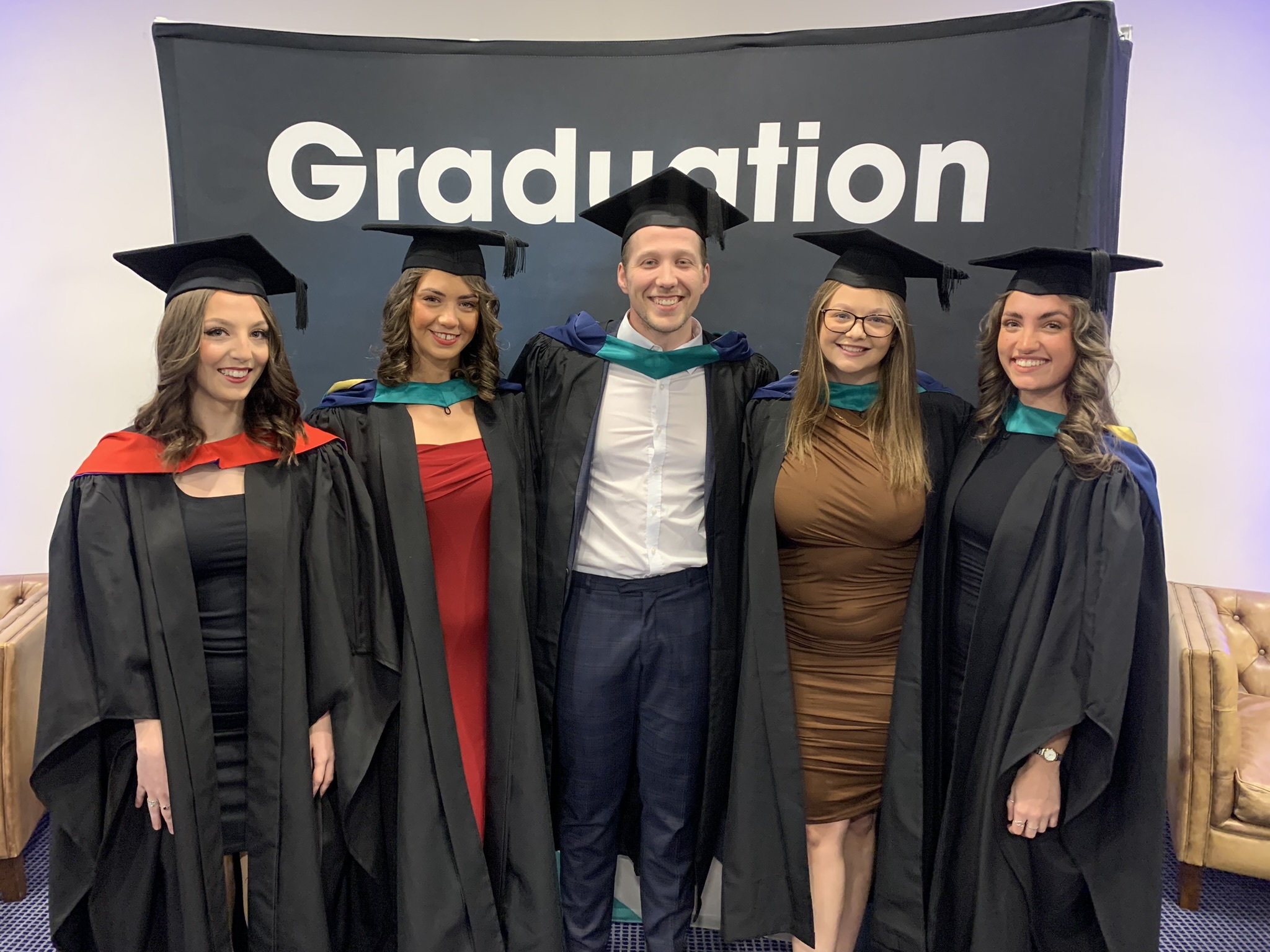 Graduates standing in front of a fabric banner with the word Graduation