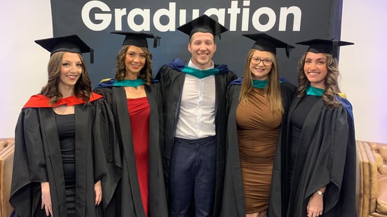 Graduates standing in front of a fabric banner with the word Graduation