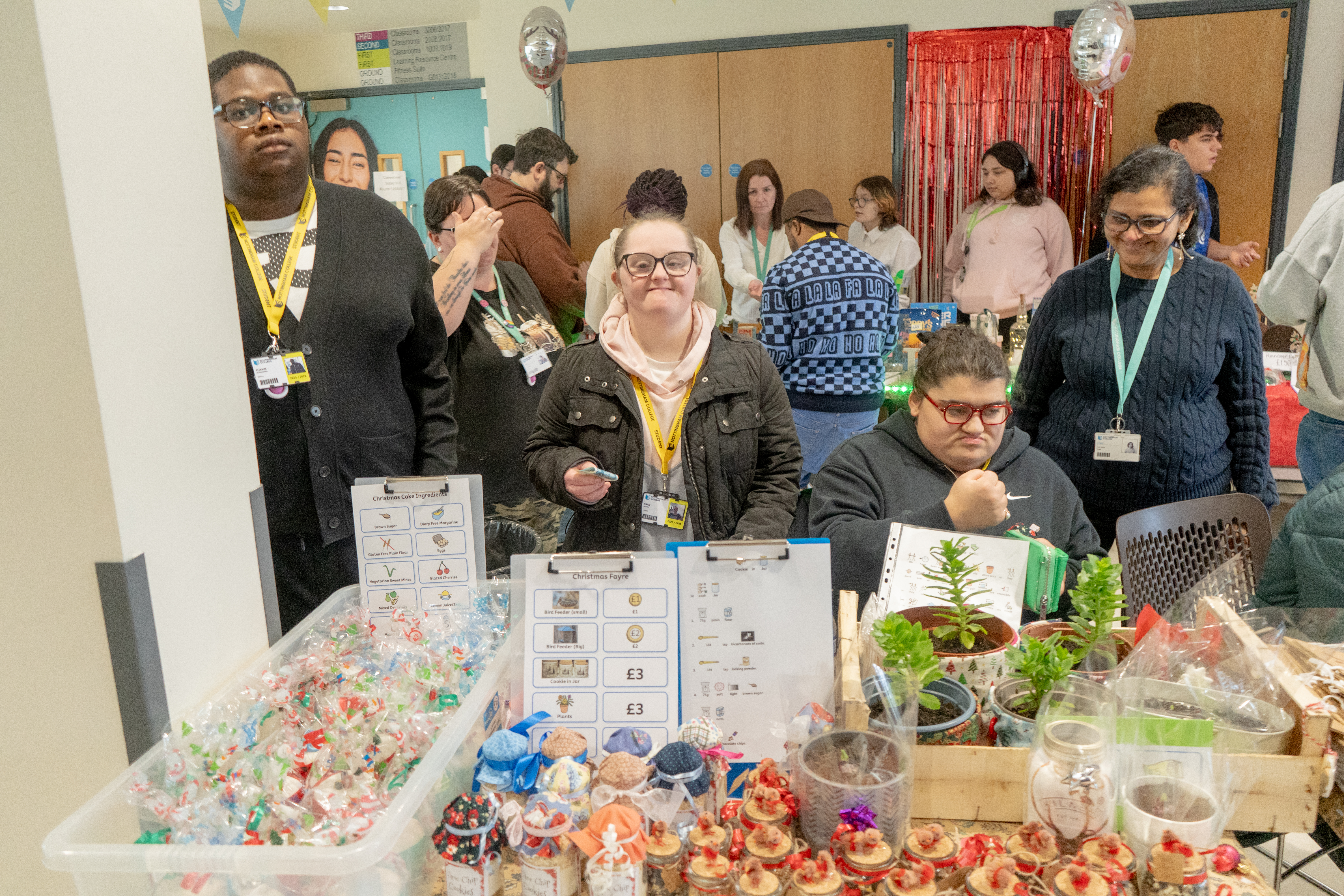 3 students and a member of staff smiling behind their stall, selling plants