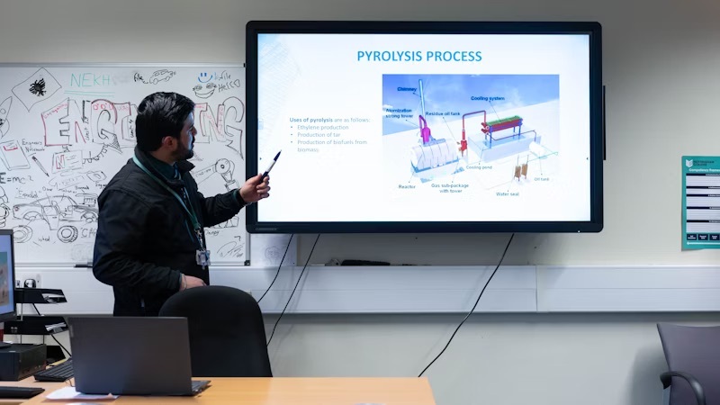 An engineering lecturer teaching pyrolysis to a class pointing at a smartboard.