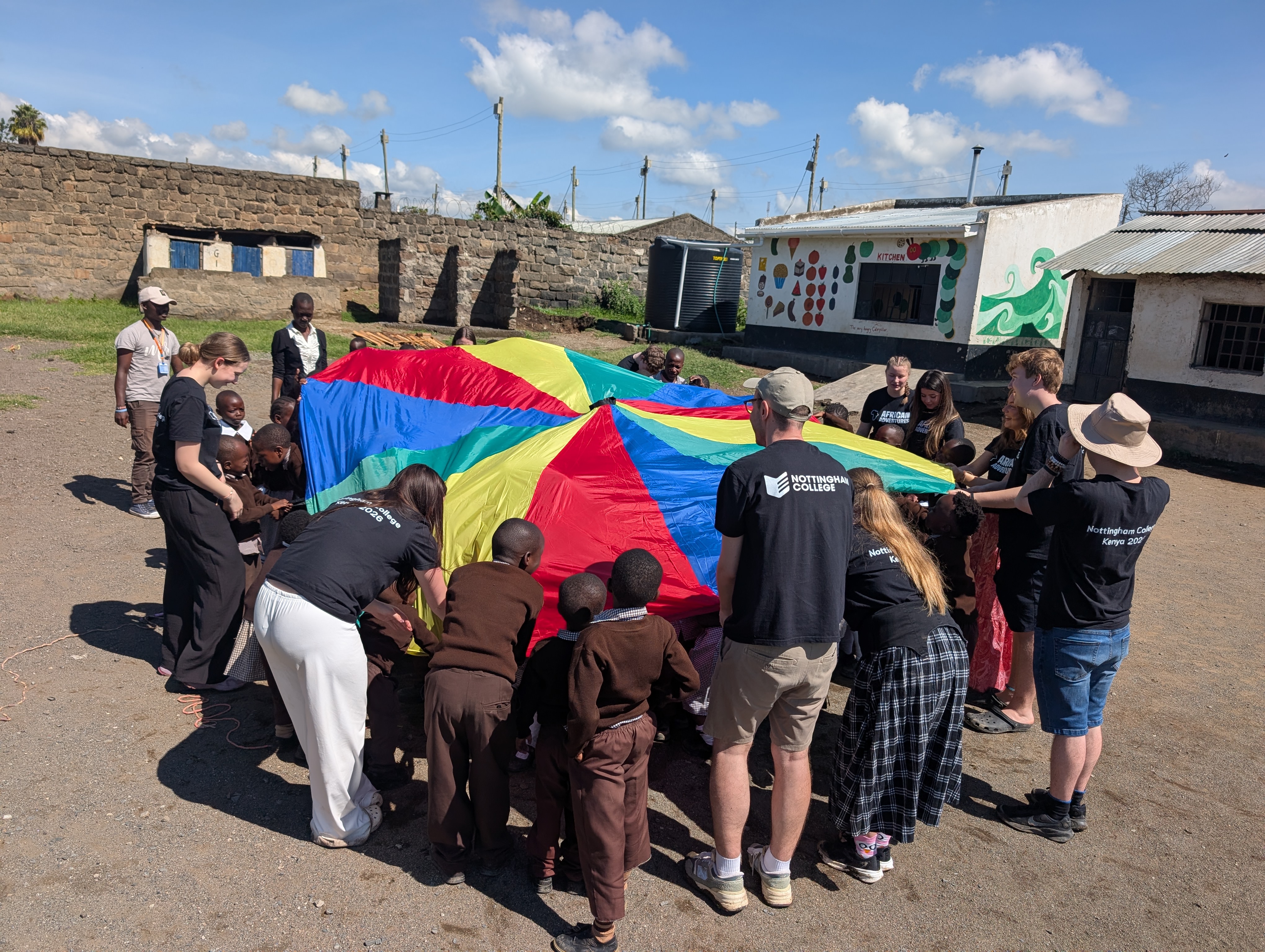 Photograph of Nottingham College students an students from Kenya playing with a colourful parachute together in a courtyard.