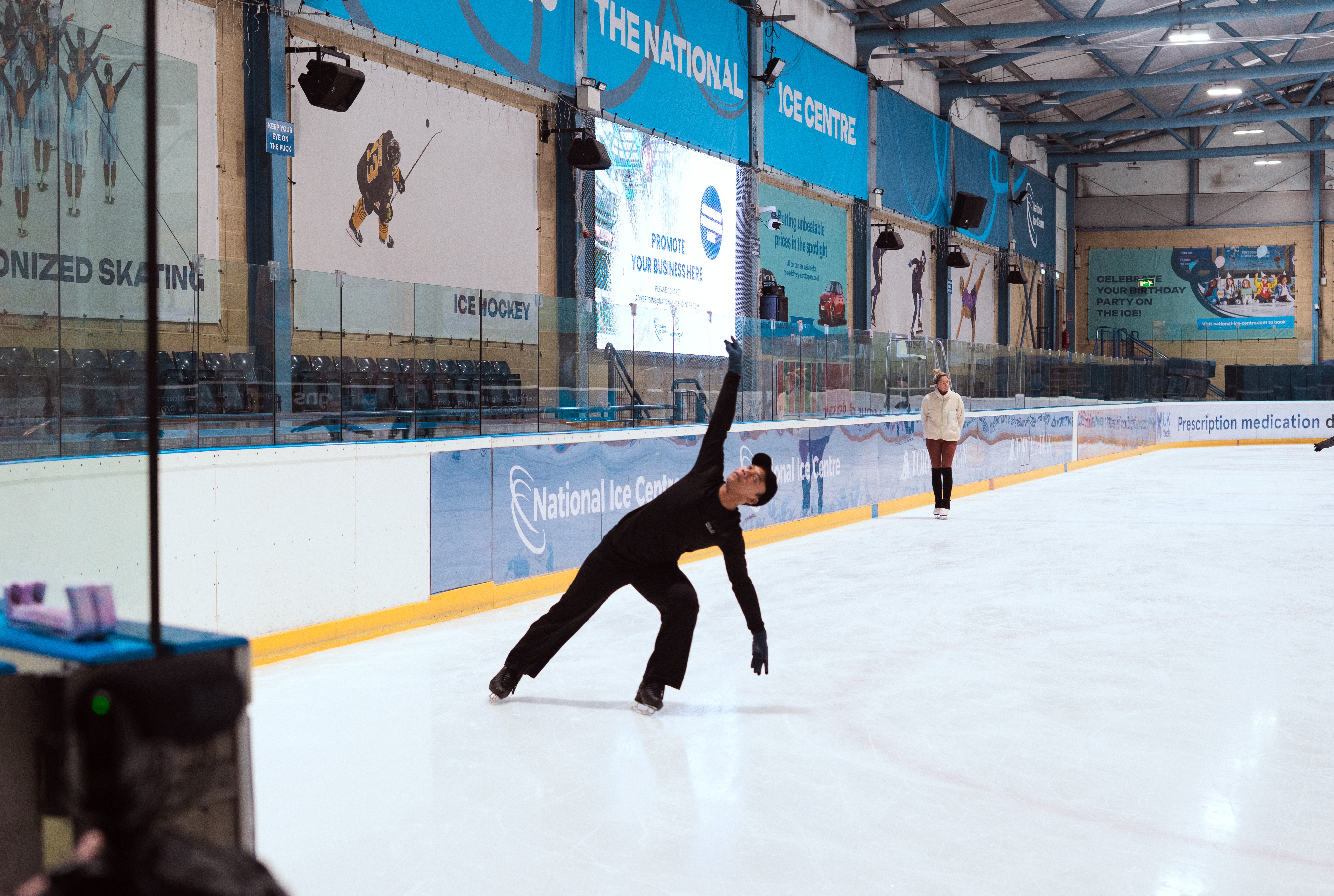 Hanyu leans down with one hand up in the air as he skates at an ice rink.