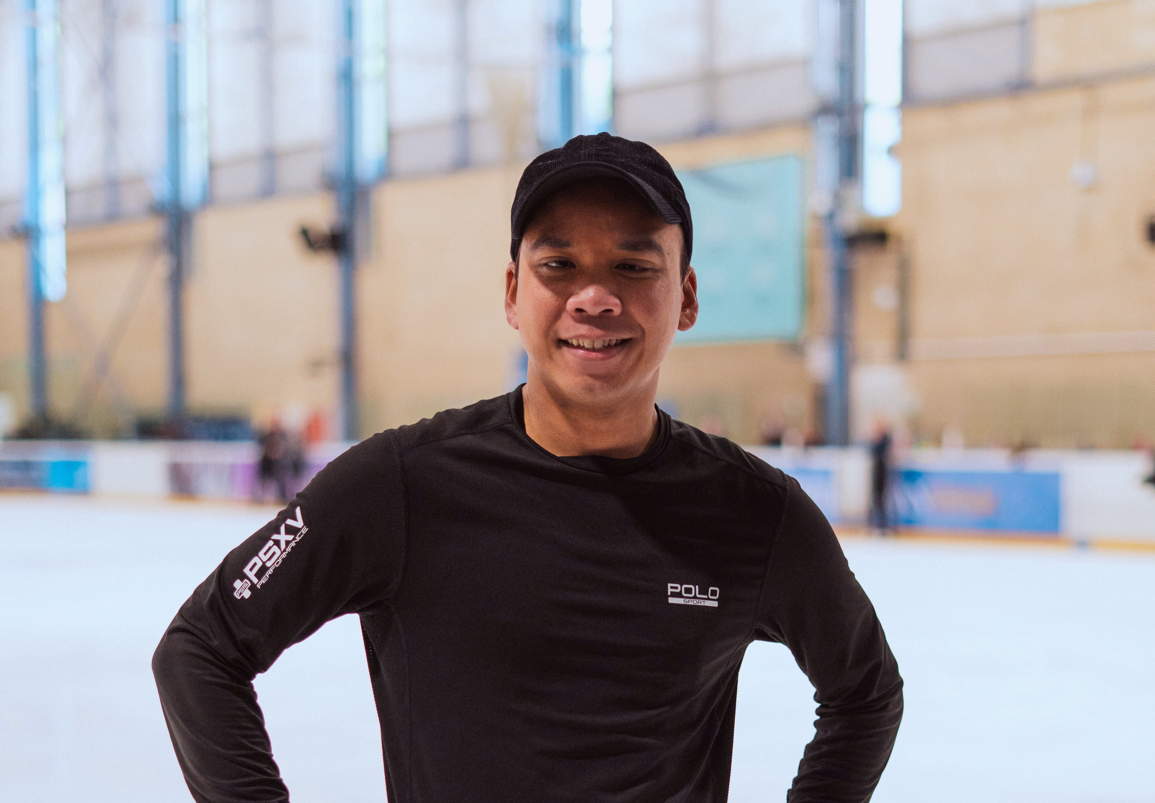 Photo of Hanyu wearing black with the ice rink behind him.