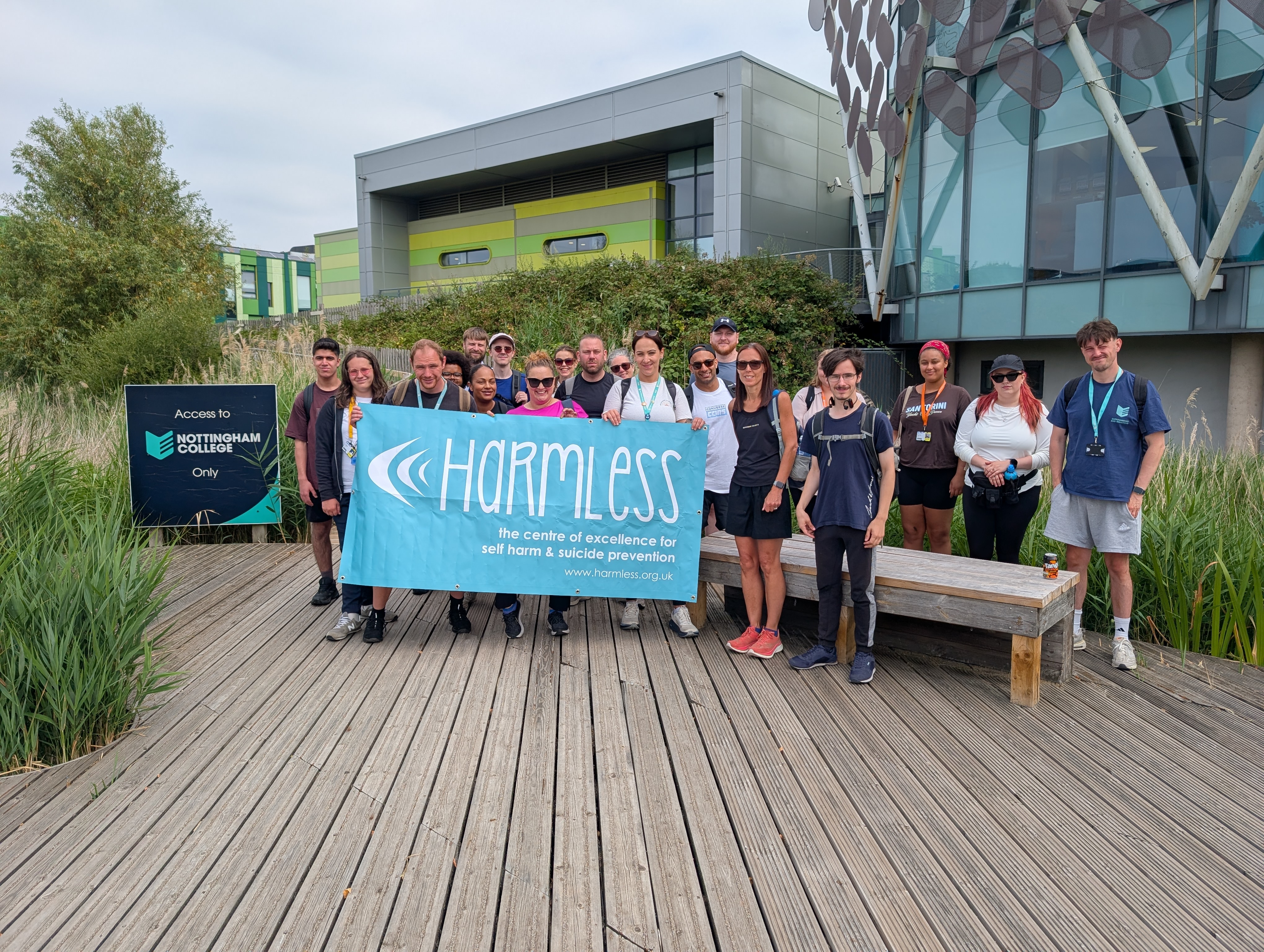 Staff and students outside Highfields holding a banner that has the charity Harmless text written on it