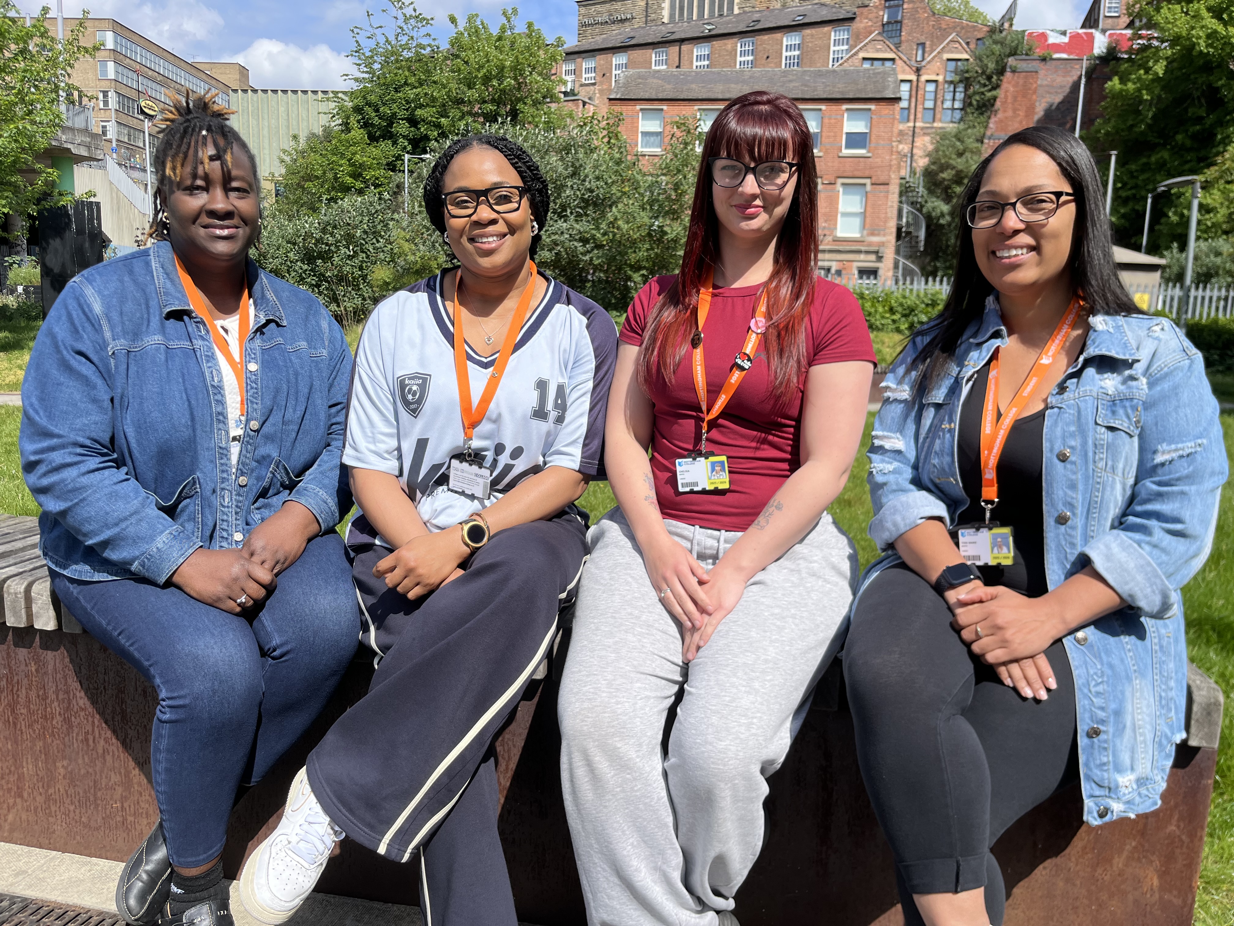 4 women sitting on a wall outdoors on a sunny day