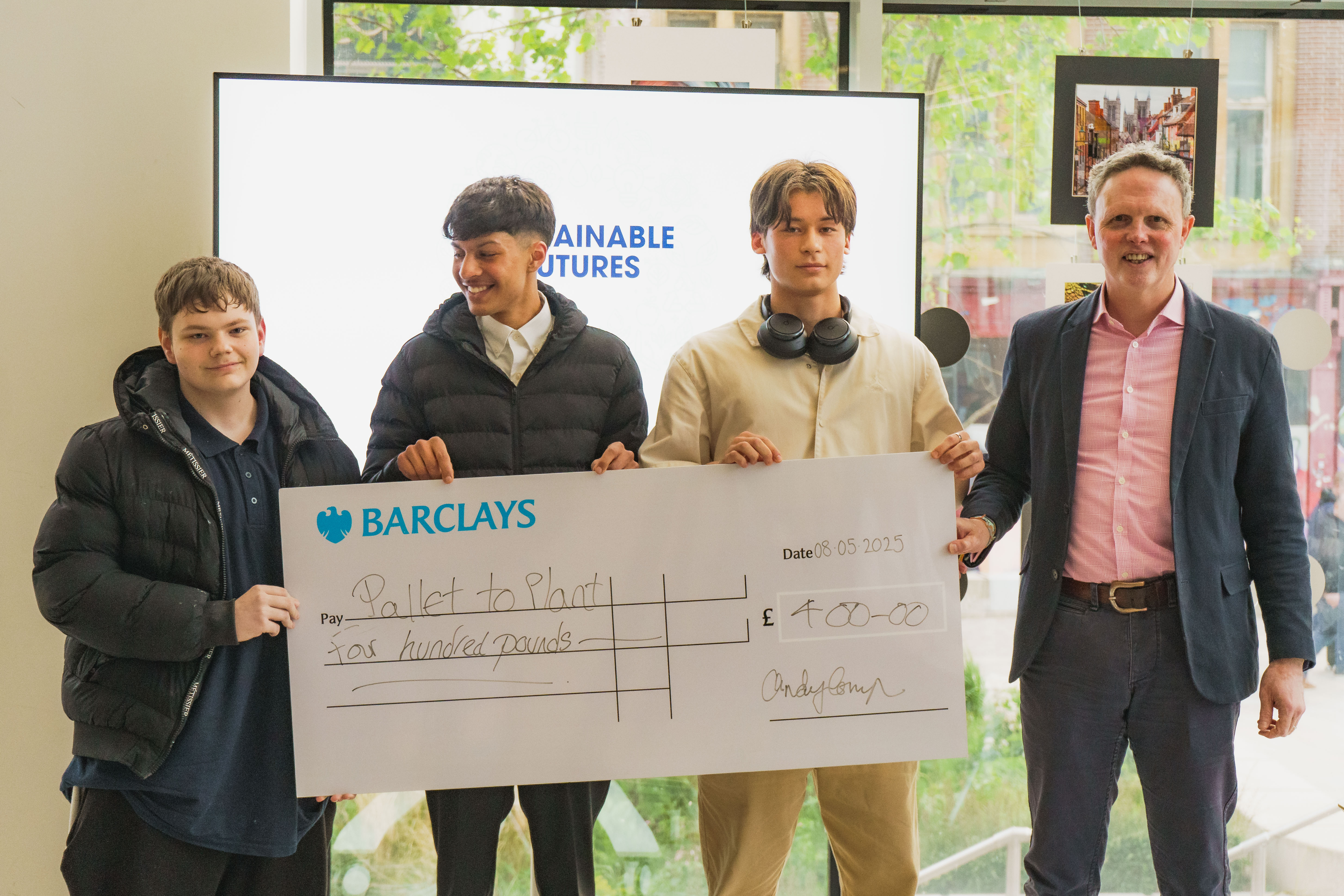 Three students smiling with a member of staff and a big cheque they were awarded