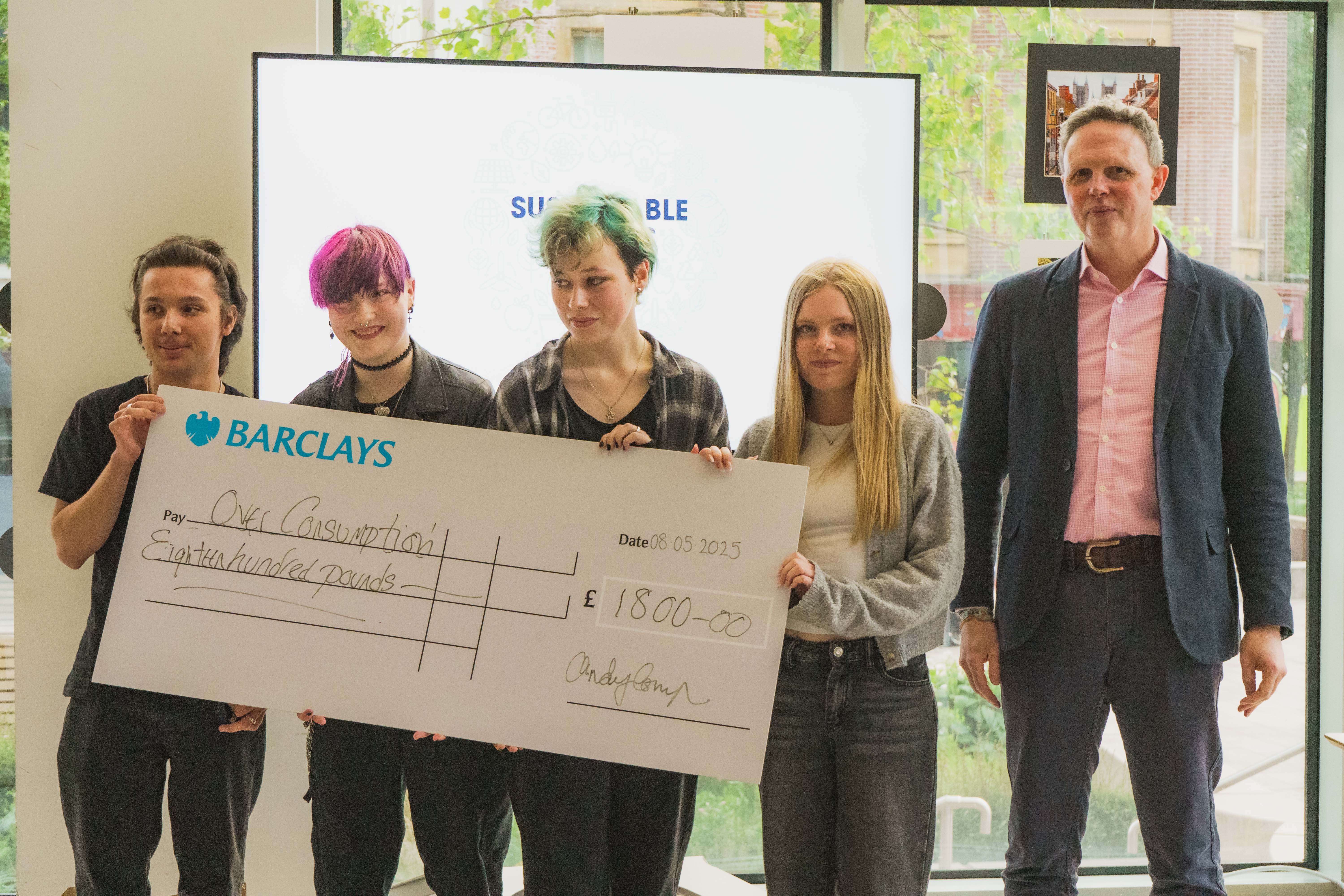Four students smiling with a member of staff and the big cheque they were awarded