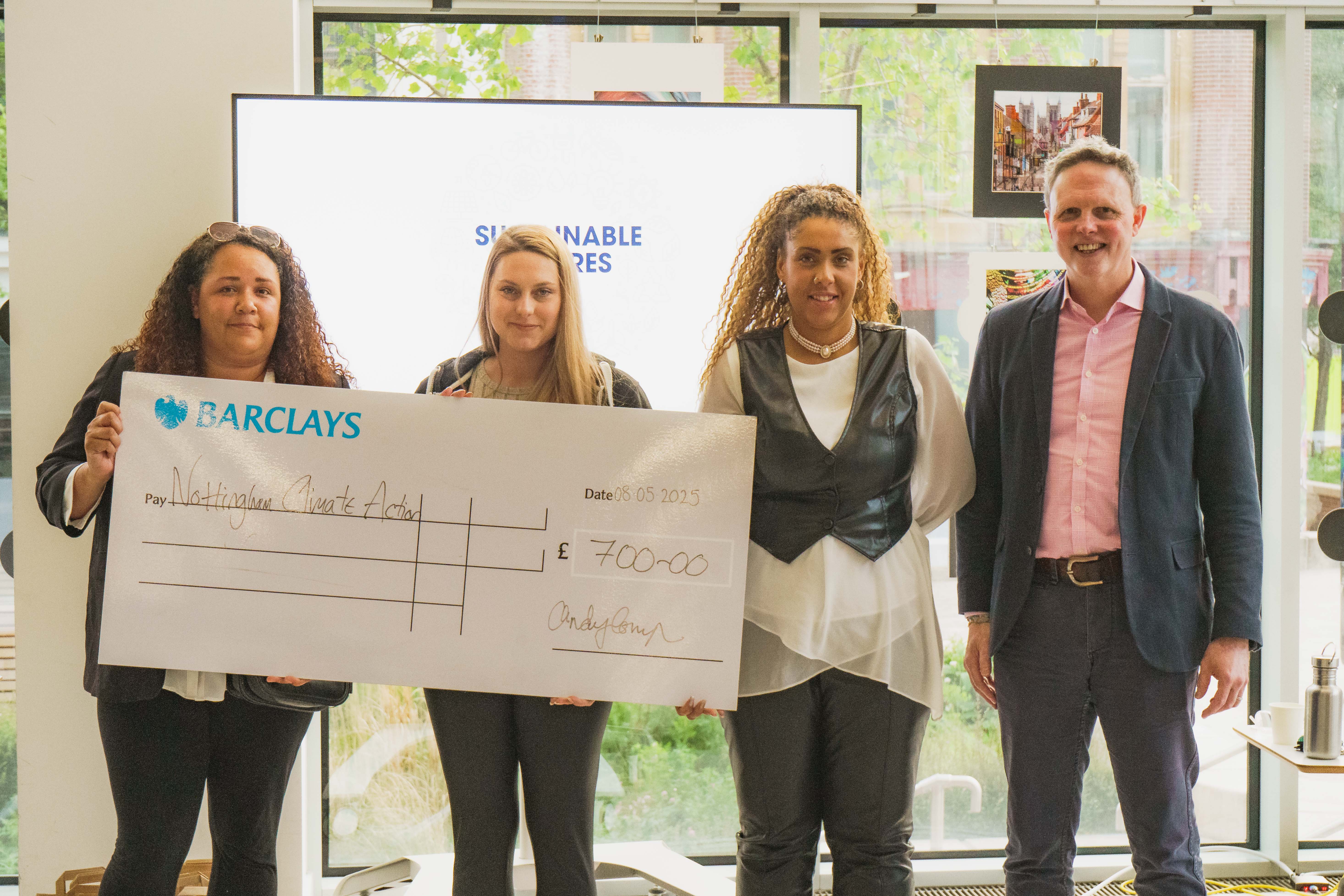 Three students smiling with a member of staff and a big cheque they were awarded