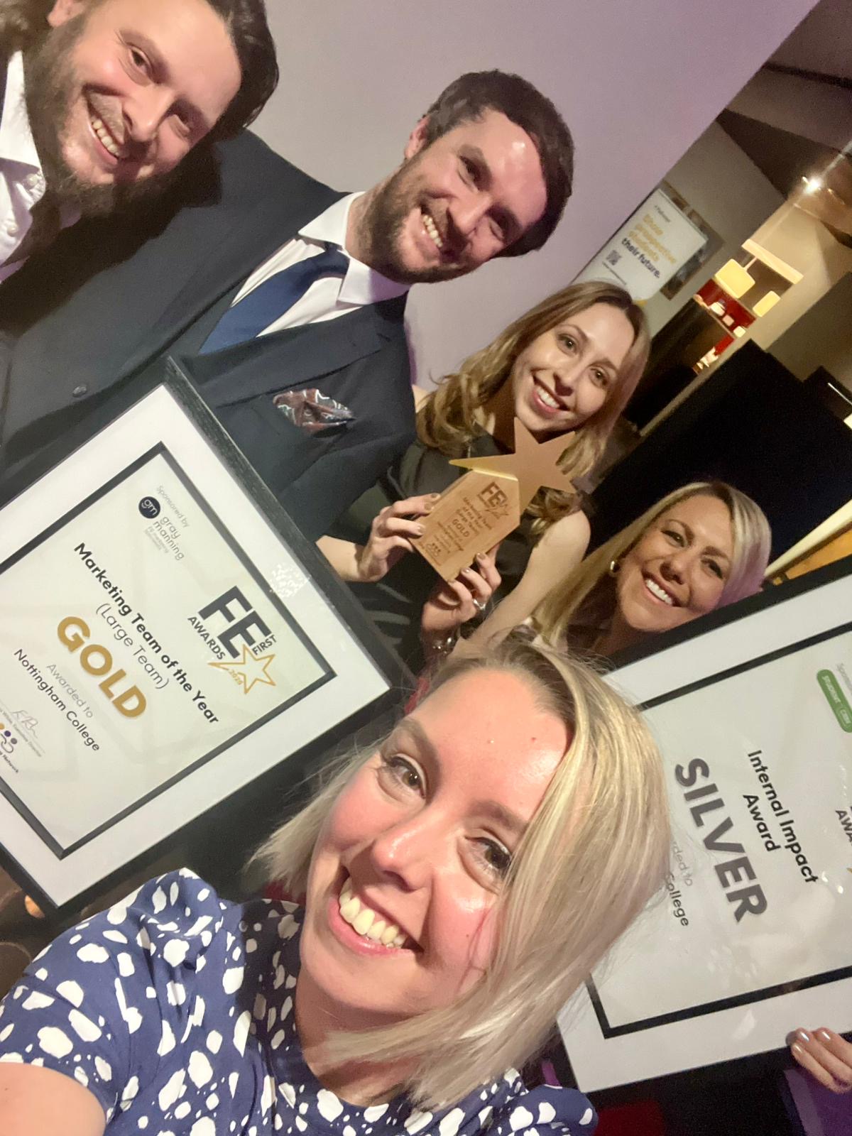 5 members of the marketing team smiling in a selfie, holding up their awards