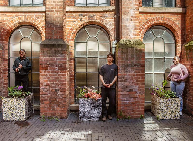 3 students stood outside next to their customised planters