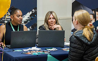 A student being helped by two members of staff at an open evening