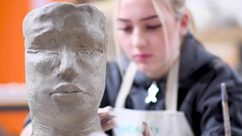 Girl with clay mould of a head in an arts class
