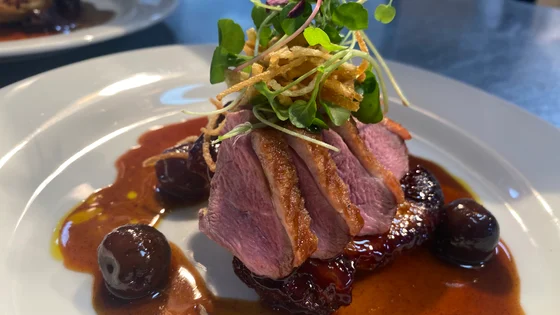 A place of seared duck with cherry sauce and salad.