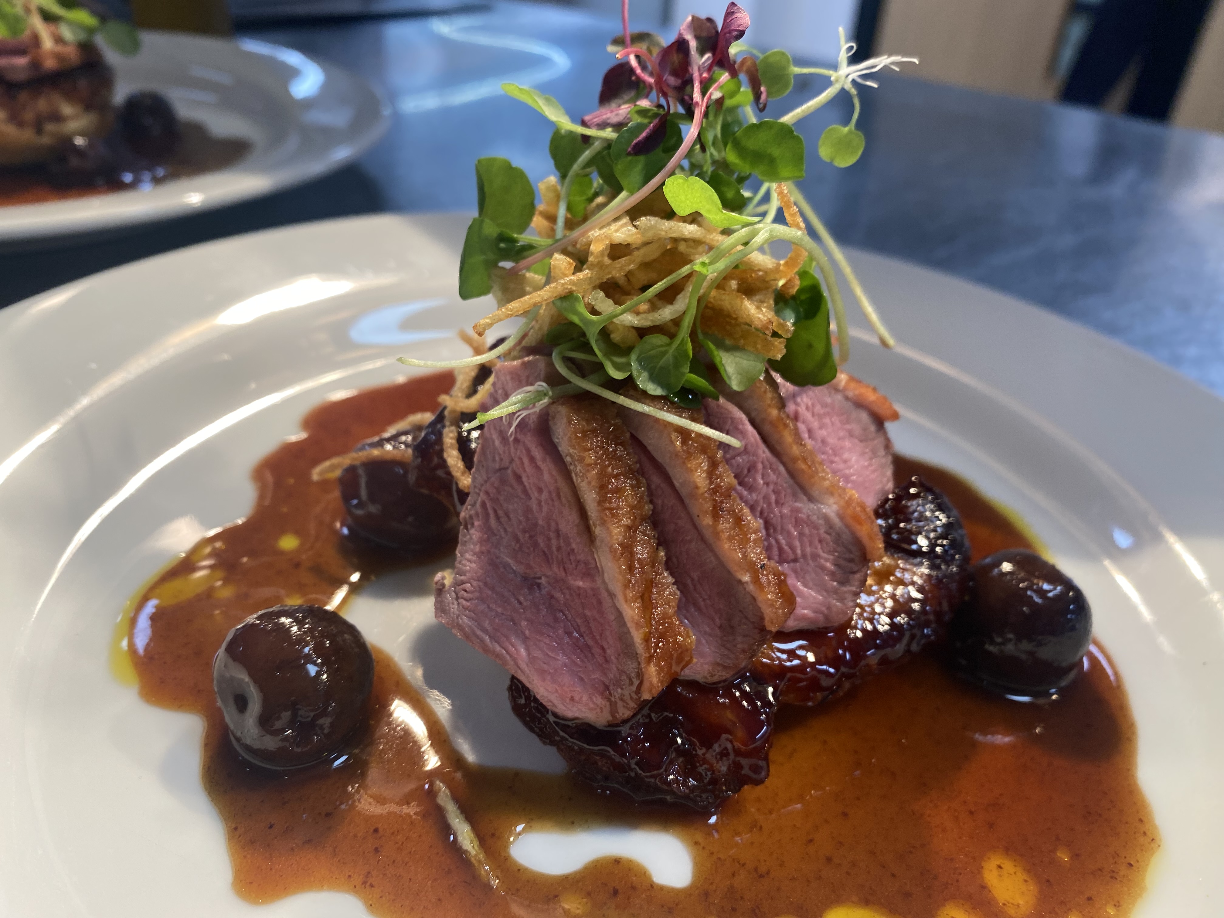 A place of seared duck with cherry sauce and salad.