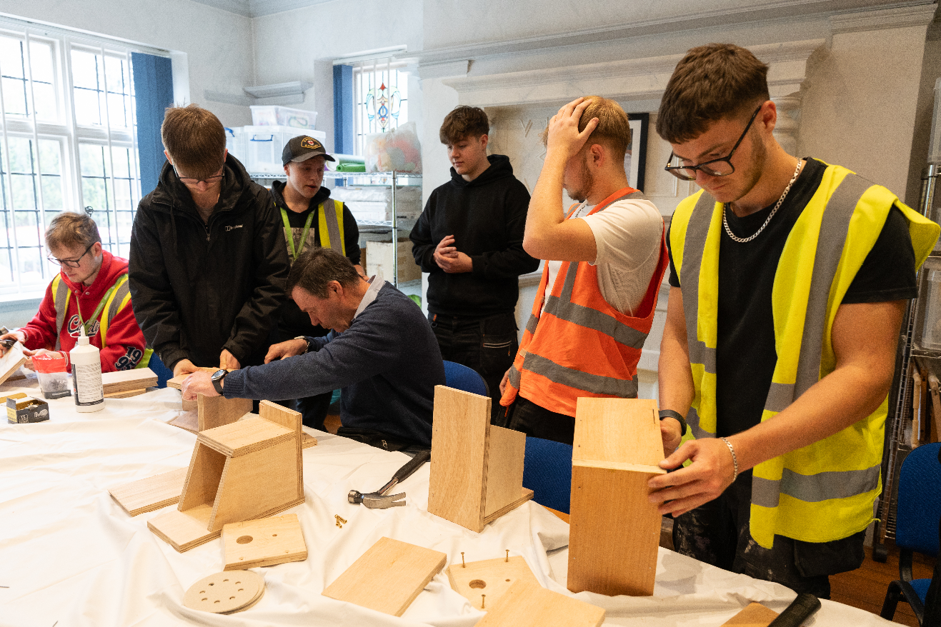 Construction students stood in a line working on wooden bird boxes