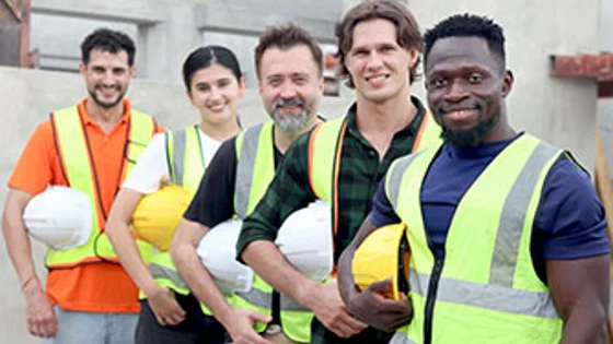A group of construction workers holding their hard hats and smiling at the camera