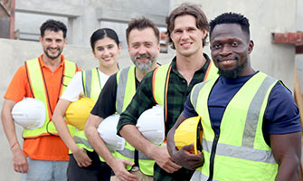 A group of construction workers holding their hard hats and smiling at the camera