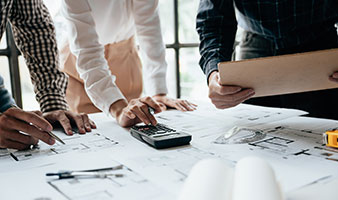 A group of students looking at architects' drawings, making notes and using a calculator.