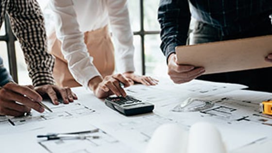 A group of students looking at architects' drawings, making notes and using a calculator.