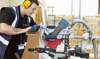 A student wearing ear defenders using a sawing machine.