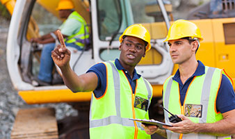 Two construction site workers talking in front of a mechanical digger.