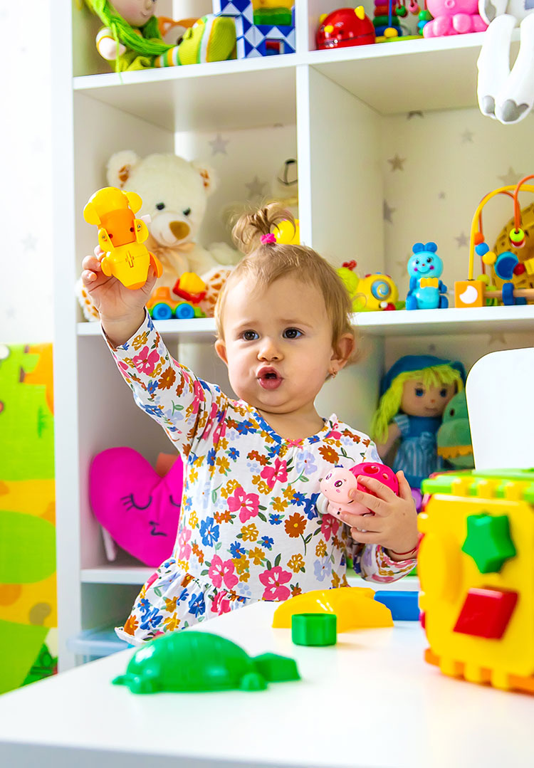 A child holding up a toy in a nursery setting.