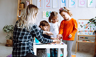 An early years educator working with three children in a nursery.