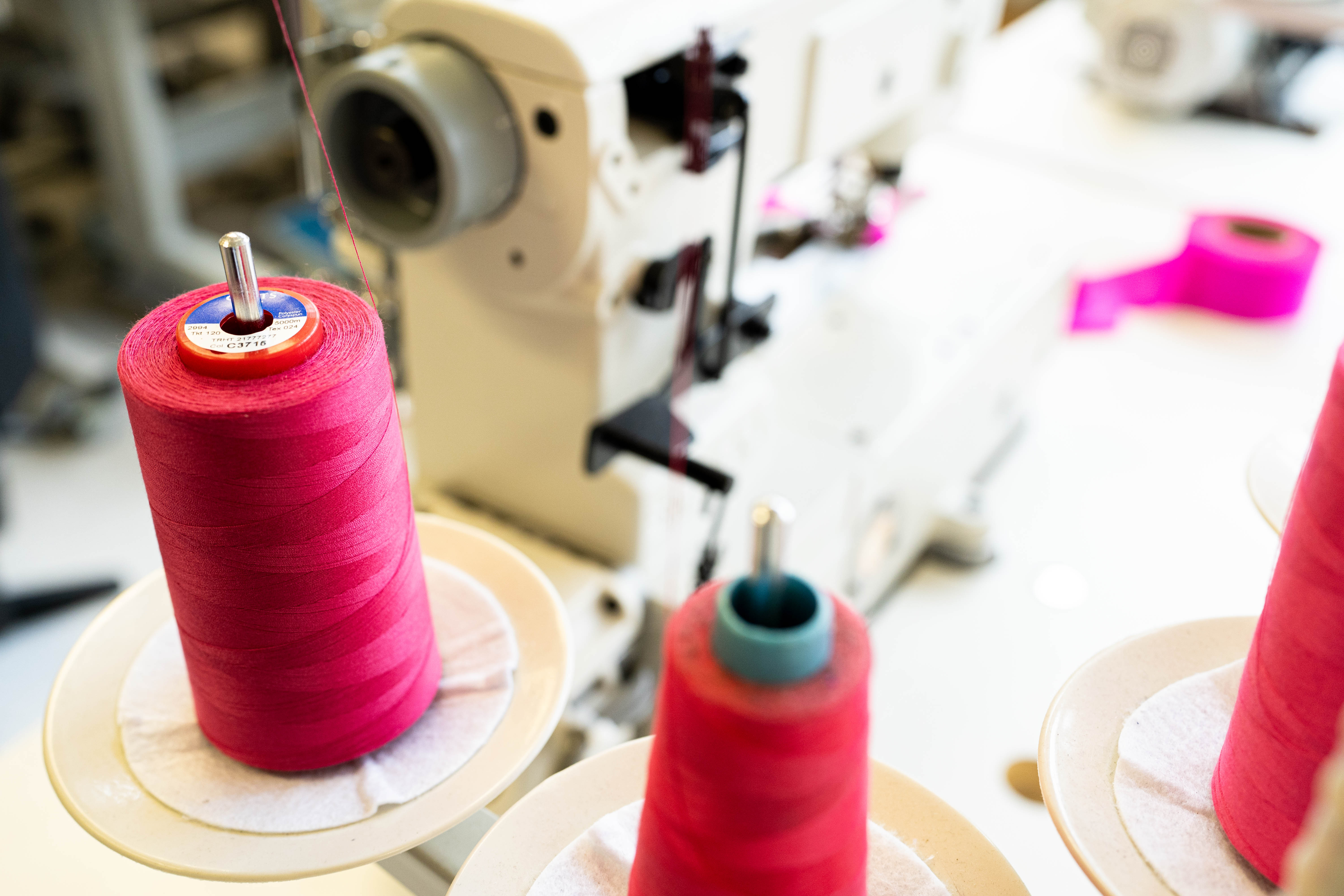 A picture of an industrial sewing machine with spool of pink and red thread