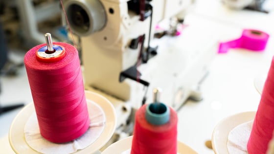 A picture of an industrial sewing machine with spool of pink and red thread