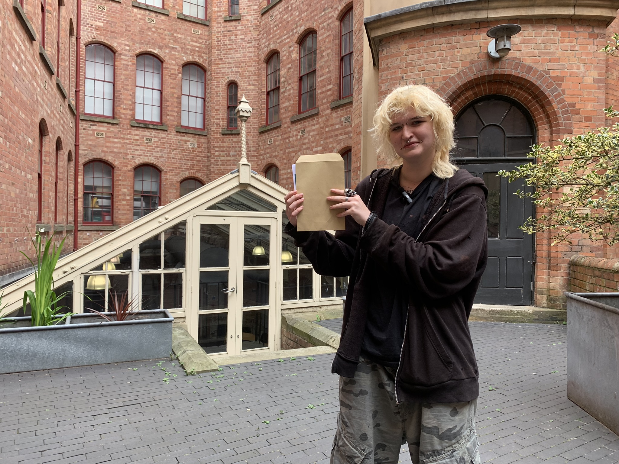 A student holding an envelope containing their GCSE results stood smiling outside