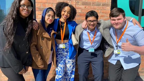 A group of smiling students stood outside of the city hub campus posing for a photo