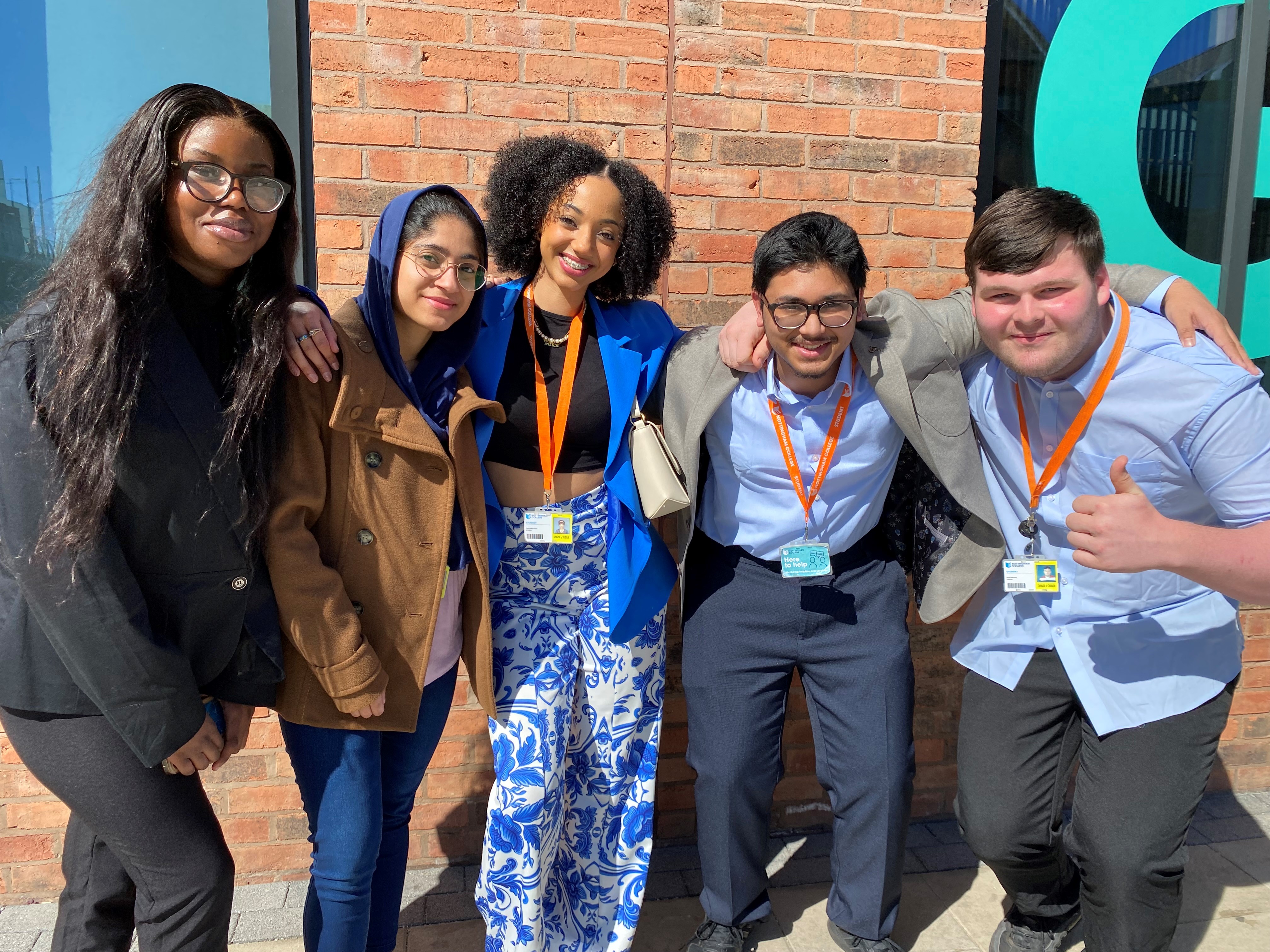 A group of smiling students stood outside of the city hub campus posing for a photo