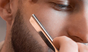 A student trimming a client's beard using a cut throat razor