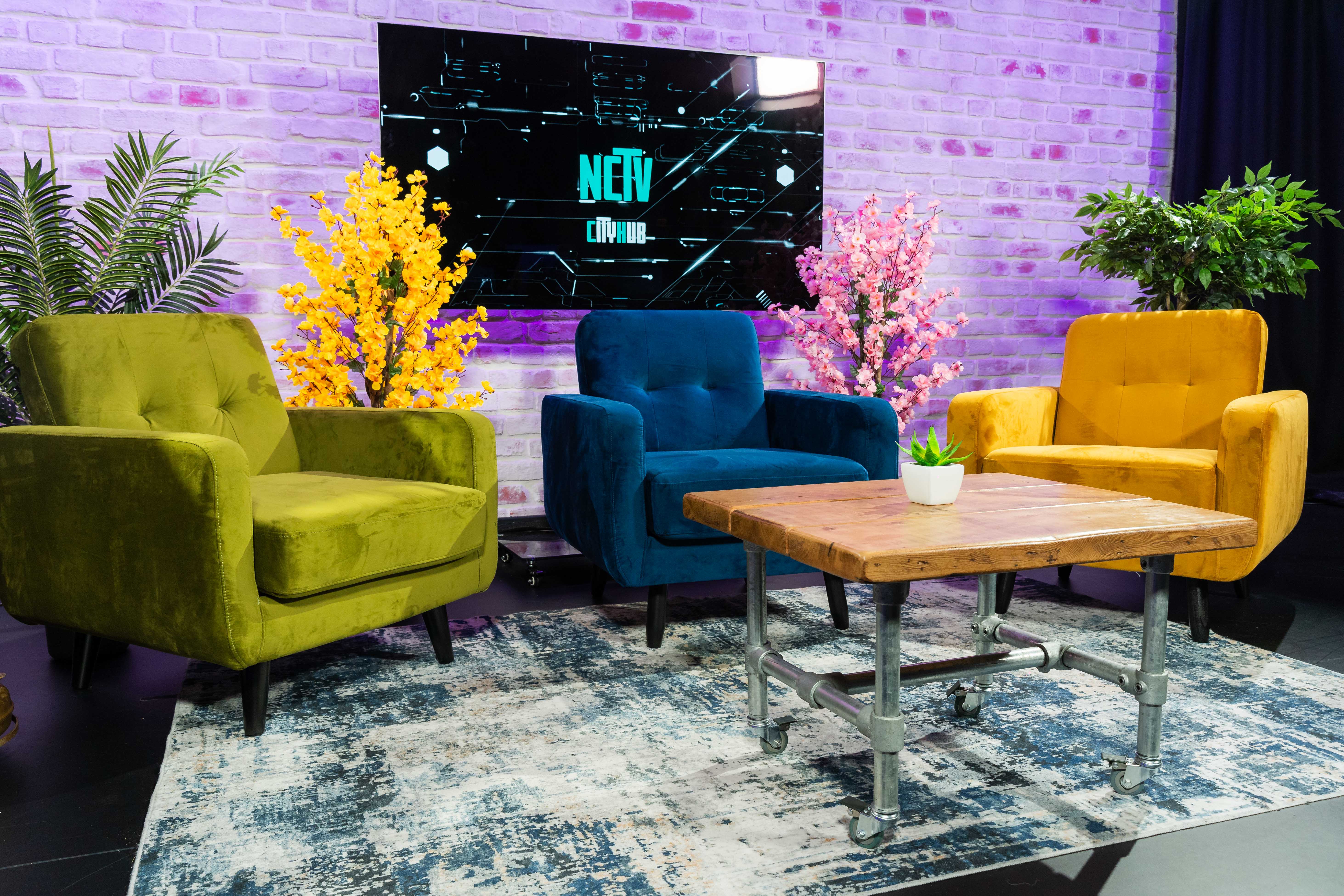 3 chairs and a table set up in front of a screen, ready for an interview