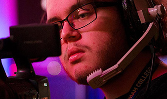 A student with a headset looking through the lens of a video camera