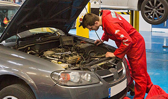 A student working on the engine of the car in an automotive workshop.