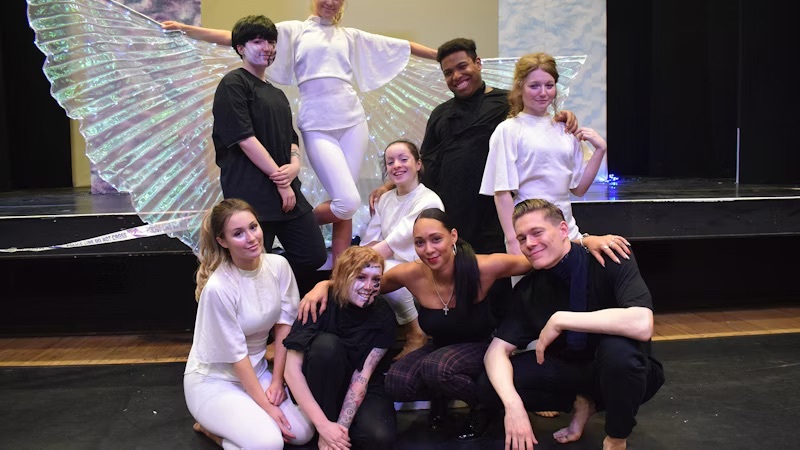 A group of students dressed in black and white posing in front of a stage