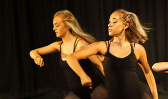 Two students dancing on stage with a black background