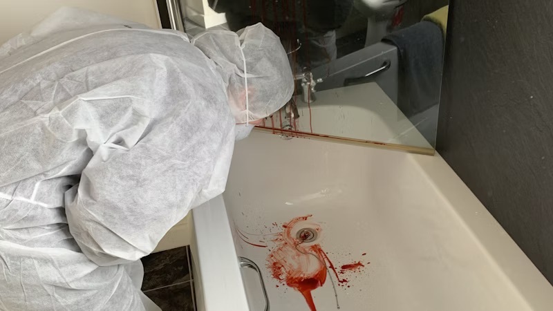 A student in protective clothing looking at blood splatter patterns in a bath at the crime scene house at Basford.